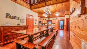 Un interior de madera con una larga mesa de comedor y bancos, una zona de cocina y una escalera.