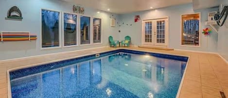 Una piscina interior con suelo de baldosas, ventanas y una puerta.
