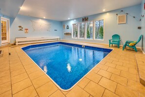 An indoor swimming pool with a tiled floor, a bench, and a window with a view of trees.