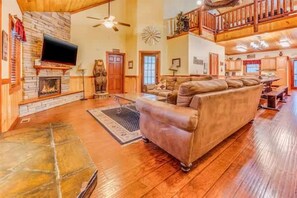 A spacious living room with a stone fireplace, a large sofa, and a high ceiling with exposed beams. - Ultimate Group Escape • Sleeps 28 • Pool • Dogs (Cosby)
