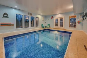 A large indoor swimming pool with clear blue water, surrounded by walls with windows and doors, and a tiled floor. - Poolin Around (Cosby)