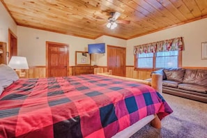Ein Schlafzimmer mit einem großen Bett, Holzboden, Fernseher und einem Fenster mit Jalousien.