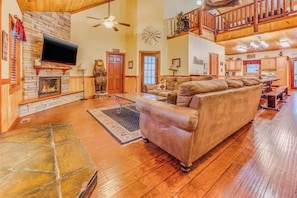 A spacious living room with a stone fireplace, a large sofa, and a high ceiling with exposed beams. - Poolin Around (Cosby)