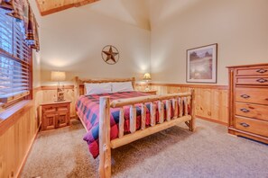 Una cama con estructura de madera y colcha escocesa, una decoración de estrella en la pared, una mesita de noche con lámpara y un aparador con cajones.