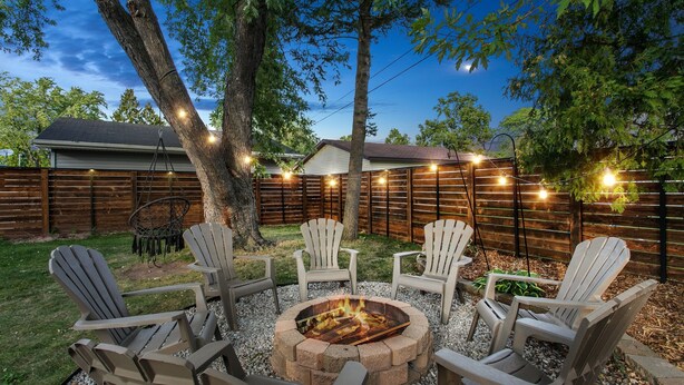 Un jardin avec un foyer, quatre fauteuils Adirondack et des guirlandes lumineuses.