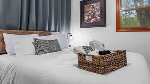 Un lit bien fait, avec du linge de lit blanc, une tête de lit en bois et un coussin à motifs noir et blanc.