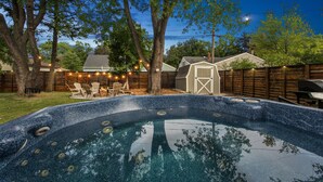 Un jardin avec un jacuzzi, une terrasse en bois, des chaises et un abri de jardin.