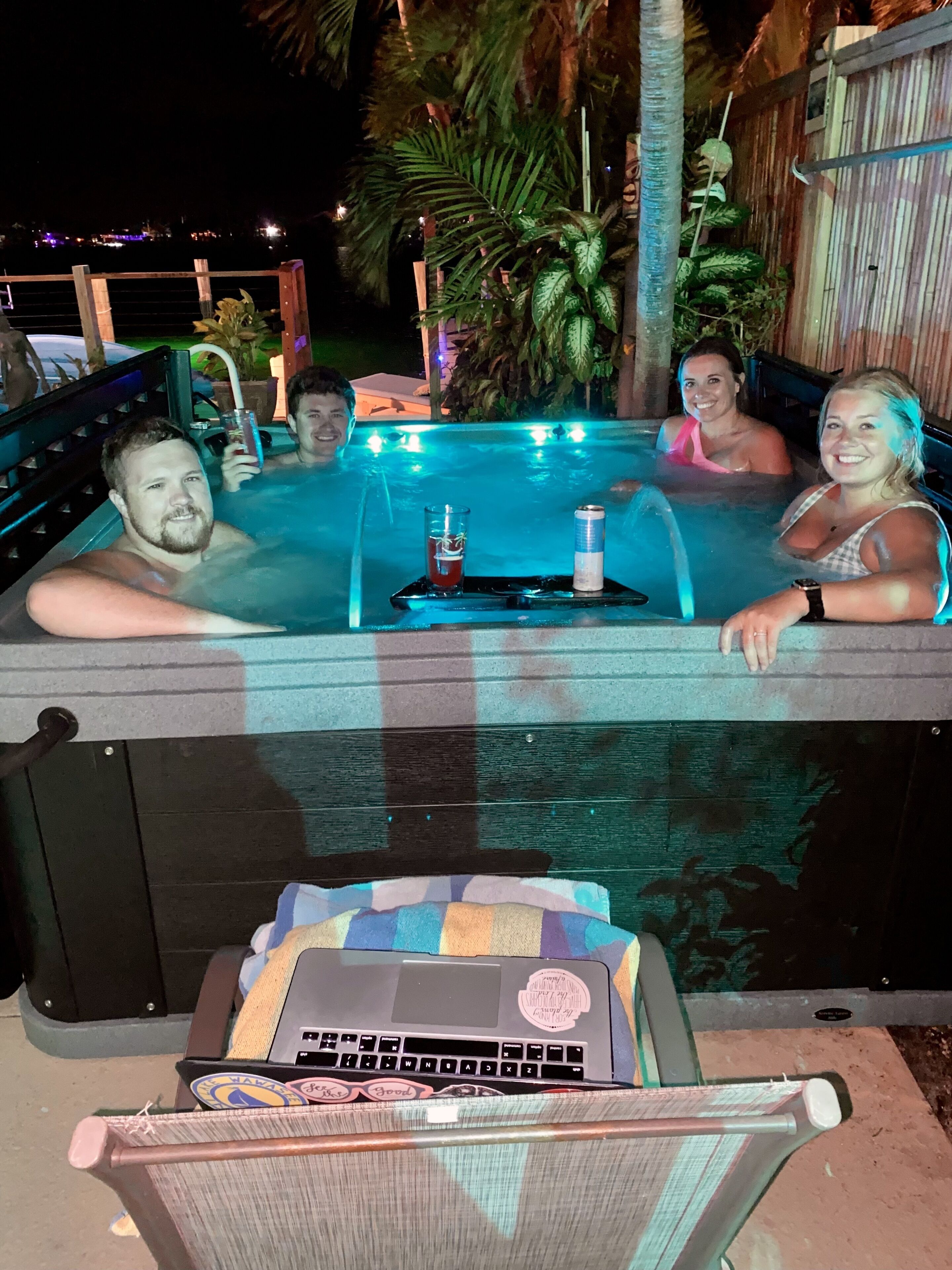 A hot tub with four people, a laptop on a chair, and a tray with drinks.