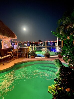 A pool area with a statue, lounge chairs, and a thatched-roof structure. - CLEAR water views @Tiki haven! Quick ocean access, Pool, HotTub, FUN! FREE ICE! (Key Colony Beach)