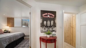 Une chambre à coucher avec un lit, une table de chevet, une lampe, une fenêtre et une affiche accrochée au mur.
