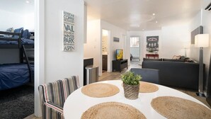 Un salon moderne avec un lit superposé, une table de salle à manger ronde avec des sets de table, un canapé et un téléviseur.