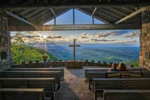 L’intérieur d’une église, avec ses bancs, un crucifix et une vue sur un paysage par une grande fenêtre.