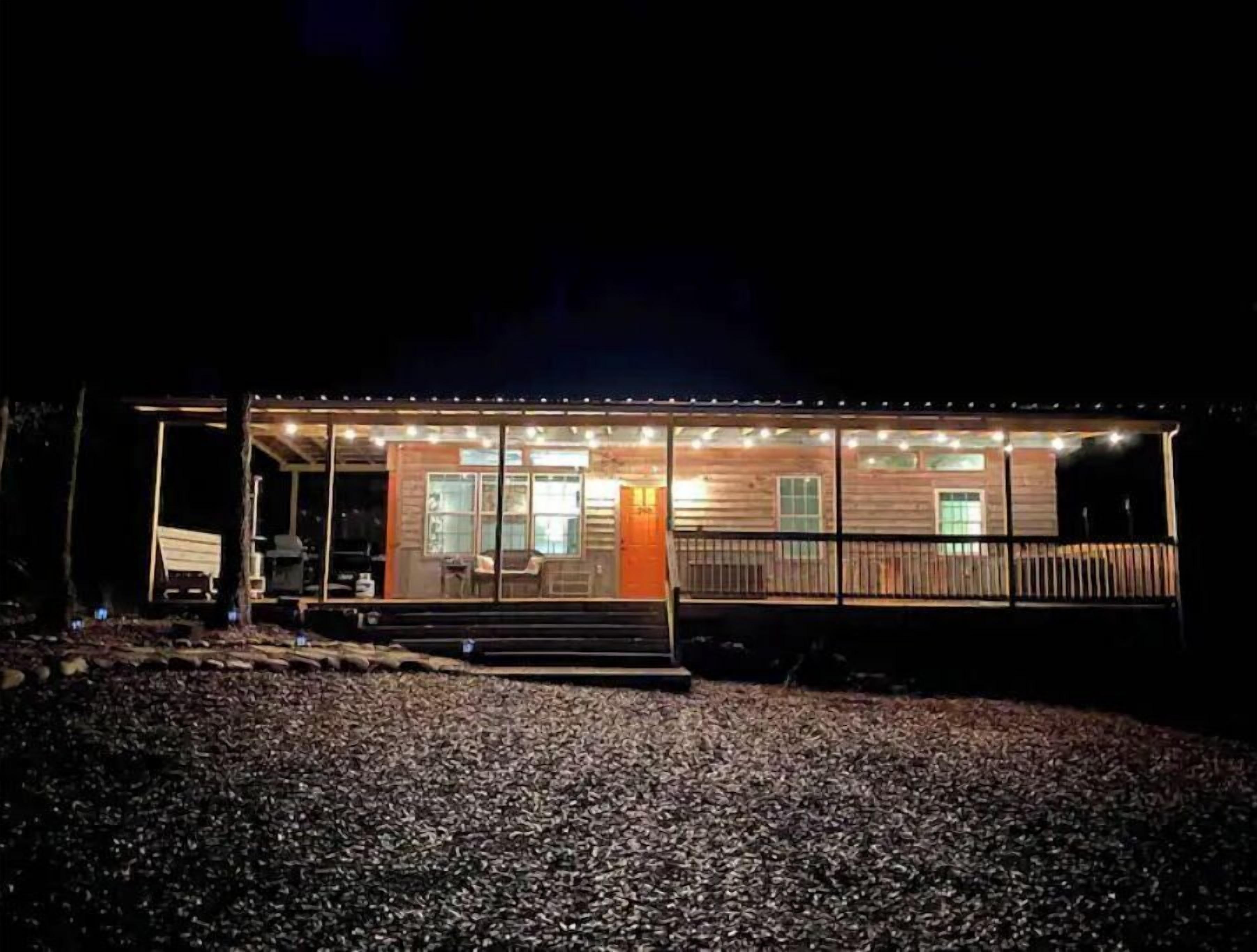 A wooden cabin with a porch, large windows, and a gravel driveway.