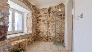 A bathroom with stone walls, a glass shower enclosure, a window, and a shelf with shoes. - Nice home in Col with house a panoramic view (Col)