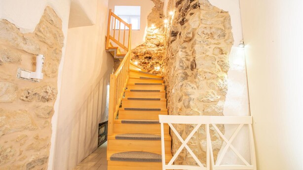 A staircase with wooden steps leading up to a landing, surrounded by stone walls and a white chair. - Nice home in Col with house a panoramic view (Col)
