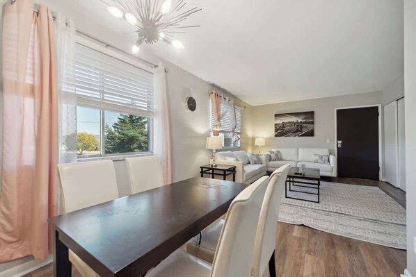 A modern living room with a dark wooden dining table, white sofas, and a patterned rug. - Fairlane #6 | Classy Cool & Chic (Lansing)