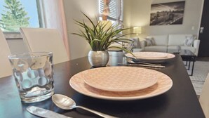 A dining table set with plates, a glass, and a spoon, with a potted plant and a painting in the background. - Fairlane #6 | Classy Cool & Chic (Lansing)