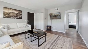 A living room with a sofa, coffee table, and artwork on the wall. - Fairlane #6 | Classy Cool & Chic (Lansing)