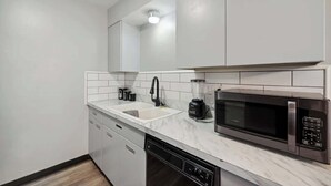 A modern kitchen with white cabinets, a sink, a black coffee maker, a blender, and a microwave. - Fairlane #6 | Classy Cool & Chic (Lansing)