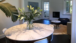 A dining area with a marble table, chairs, a vase with flowers, and a large plant.