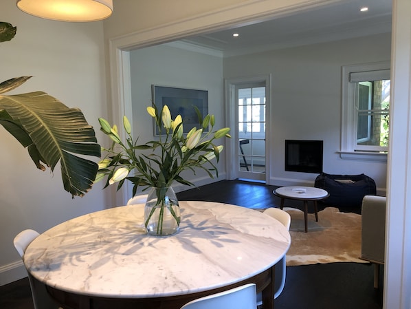 Un coin repas avec une table en marbre, des chaises, un vase de fleurs et une grande plante.