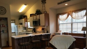 A cozy kitchen with a bar area, wooden cabinets, and a large window with sheer curtains.