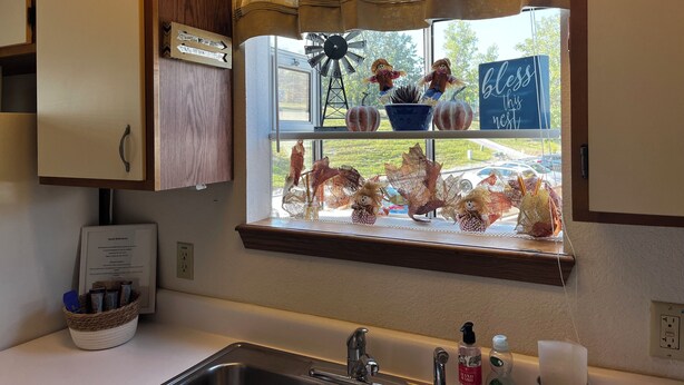 A kitchen with a window, a sign reading "Bless is this nest", and a sign with arrows.