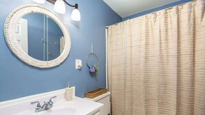 Ein Badezimmer mit einem runden Spiegel, einem weißen Waschbecken, einer Toilette und einem beige gefärbten Duschvorhang.