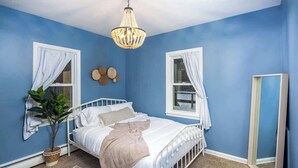 Ein Schlafzimmer mit einem weißen Metallbett, einer Pendelleuchte, einer Topfpflanze und einem Spiegel.