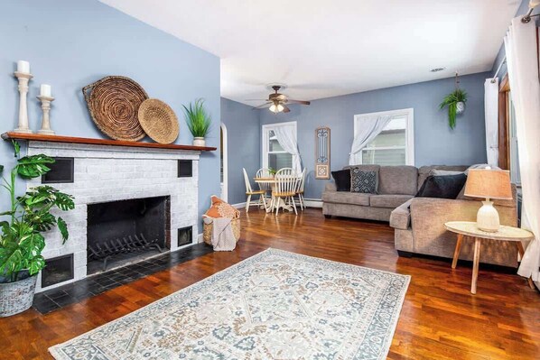 A living room with a fireplace, a sofa, a dining table with chairs, and a ceiling fan.