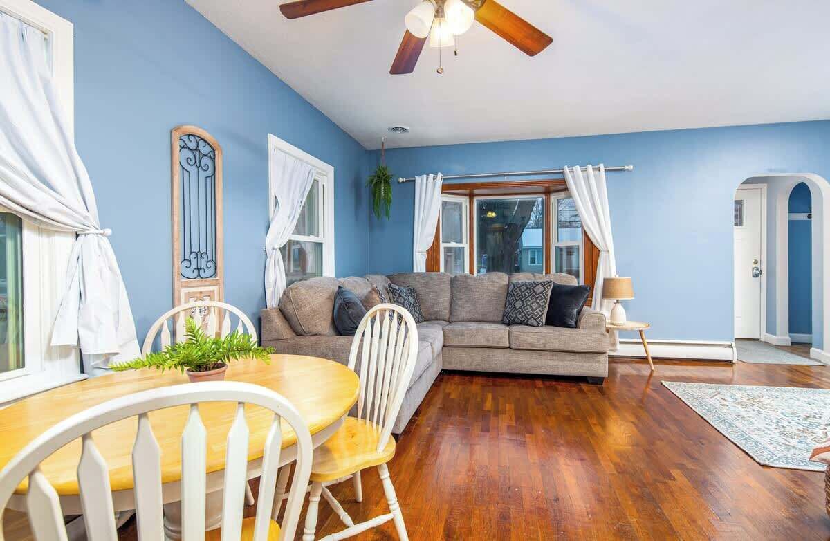 A living room with a sofa, dining table, chairs, and a ceiling fan.