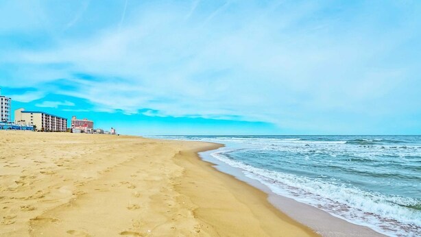 Une plage avec un rivage sablonneux, des vagues de l’océan et des bâtiments en arrière-plan.