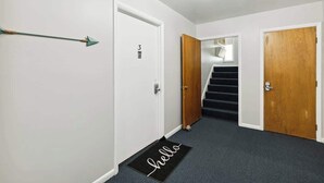Ein Flur mit Fußmatte, einer Tür mit Hausnummer und einer Treppe.