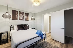 A bedroom with a bed, two wall-mounted lamps, a door, and a small bedside table.
