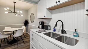 Eine moderne Küche mit weißen Schränken, einer Spüle, einer Kaffeemaschine, einem Toaster und einer Pendelleuchte.