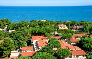 Ein Küstenwohngebiet mit Häusern mit roten Ziegeldächern, umgeben von dichtem Grün und Blick auf das Meer.