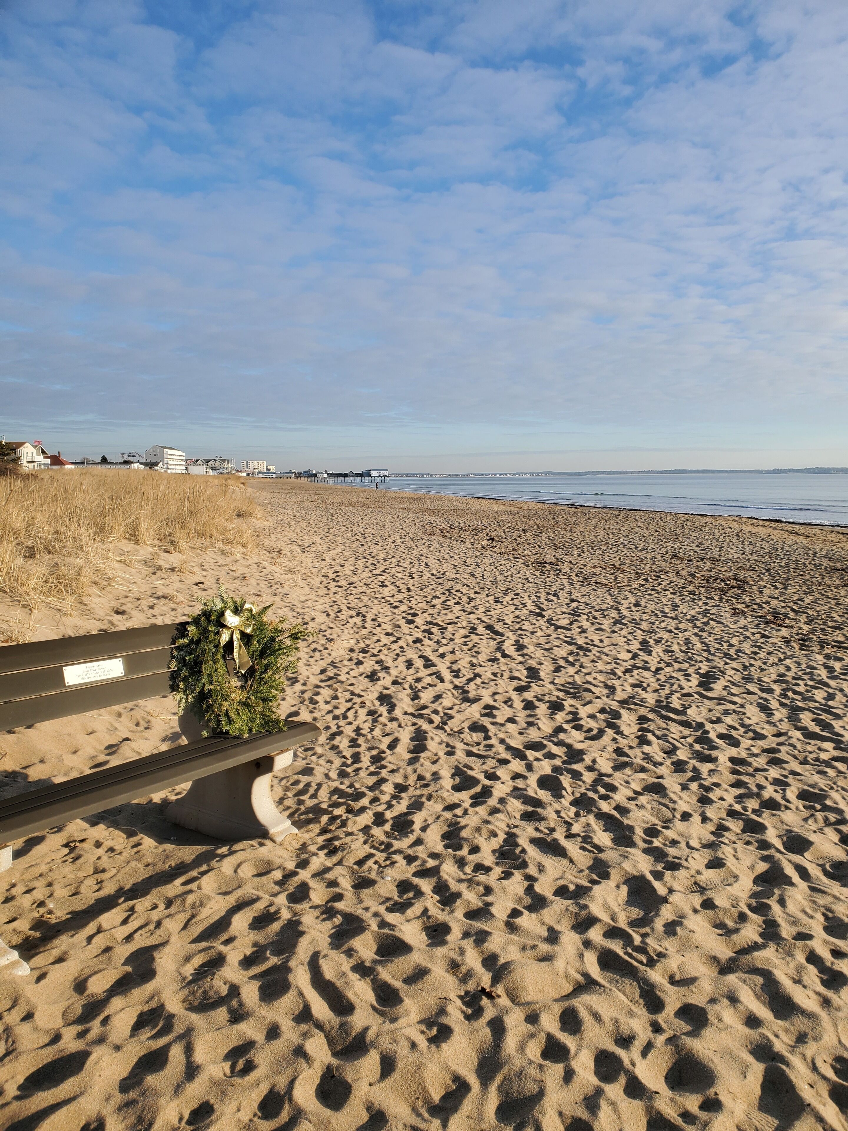 Uma praia arenosa com pegadas, um banco e um guirlanda de Natal.