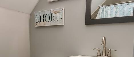 A bathroom with a toilet, a sink with a mirror above it, and two signs on the wall reading "BEACH" and "SHORE".