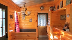 A log cabin interior with a wooden bench, a dining table with chairs, a chandelier, and a fireplace. - Pet friendly, hot tub, cabin (Luther)