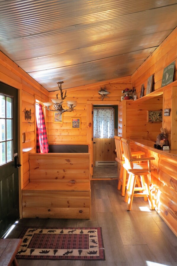 A log cabin interior with a wooden bench, a dining table with chairs, a chandelier, and a fireplace.