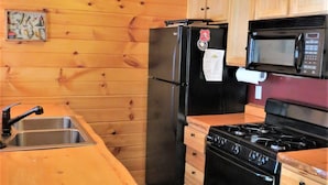 A compact kitchen with wooden cabinets, a refrigerator, a microwave, and a stove. - Pet friendly, hot tub, cabin (Luther)