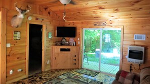 A cabin interior with a mounted deer head, a ceiling fan, a television, and a sliding glass door to the outdoors. - Pet friendly, hot tub, cabin (Luther)