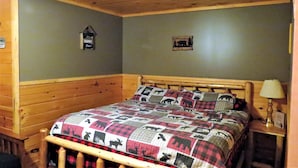 A wooden bed with a quilt featuring animal prints, a nightstand with a lamp, and a wall with two signs. - Pet friendly, hot tub, cabin (Luther)