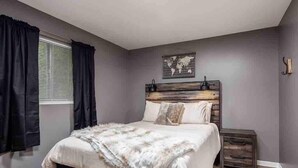 Un dormitorio con cama, mesita de noche, ventana con cortinas y un mapa del mundo en la pared.