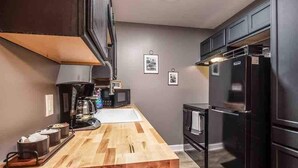 Una cocina moderna con encimera de madera, cafetera, microondas y refrigerador negro.