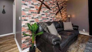 Una sala de estar con pared de ladrillo, un sofá de cuero oscuro y una planta en maceta.