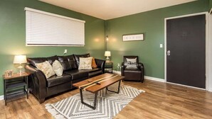 A living room with a sofa, coffee table, and two lamps. - Fairlane #8 | The Den (Lansing)