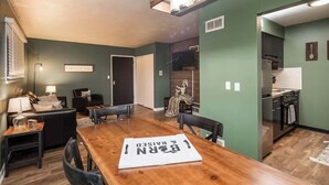 A dining area with a wooden table, chairs, and a sign on the table. - Fairlane #8 | The Den (Lansing)