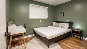 A bedroom with a bed, bedside table, and a desk with a chair. - Fairlane #8 | The Den (Lansing)