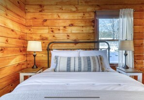 A wooden cabin room with a metal bed frame, two bedside lamps, a window with curtains, and a view of a snowy landscape. - Clean Secluded Cabin w/ Incredible Mountain Views! (Mexico)